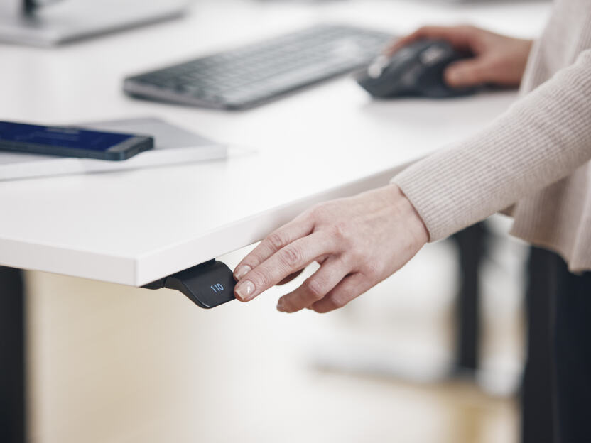 A woman touching the Linak desk controller to adjust the height of the ATS table by Faust.