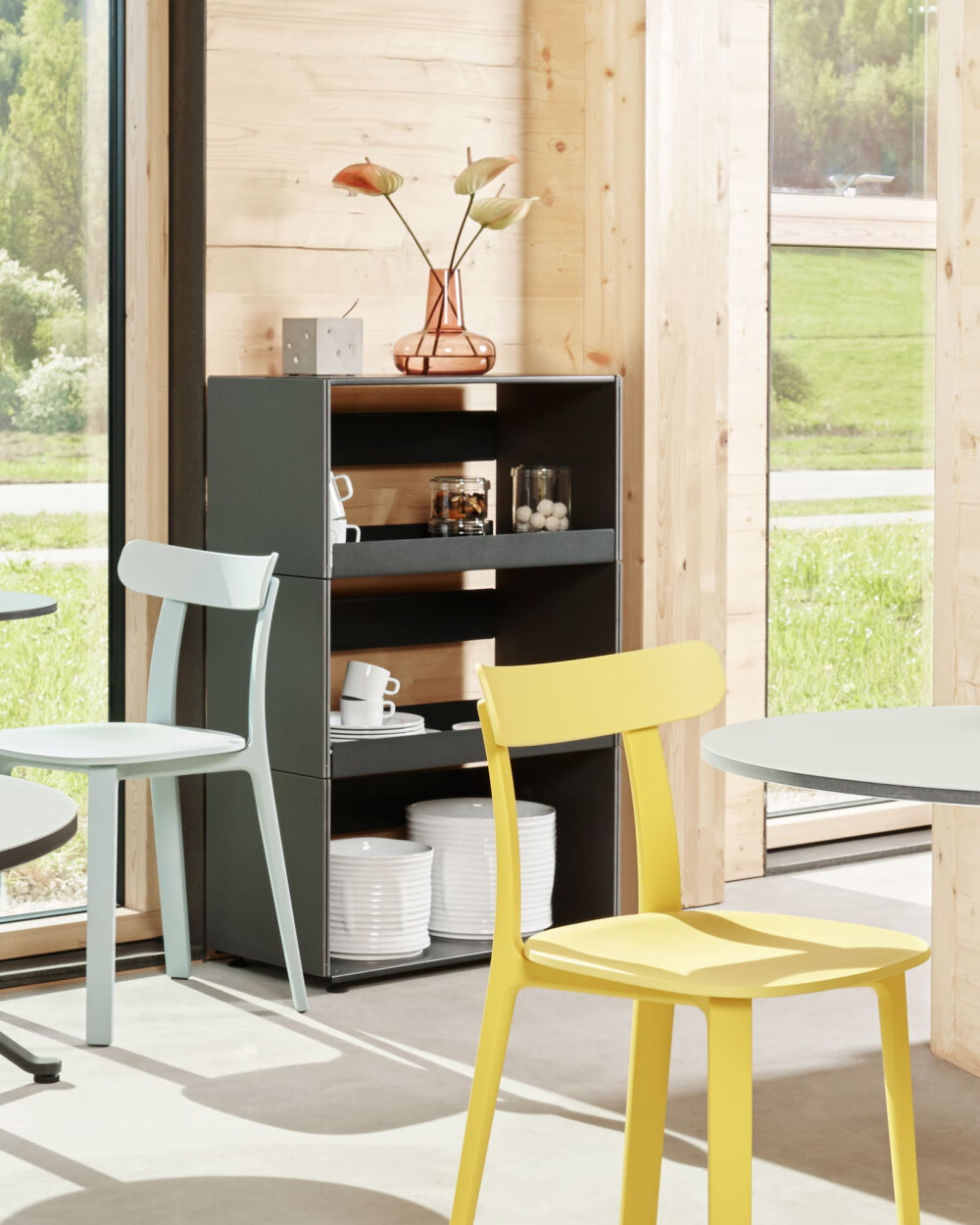 Plus Minus shelf by Faust made of black linoleum, stocked with crockery and a vase, in front of a wooden wall with a large window front.