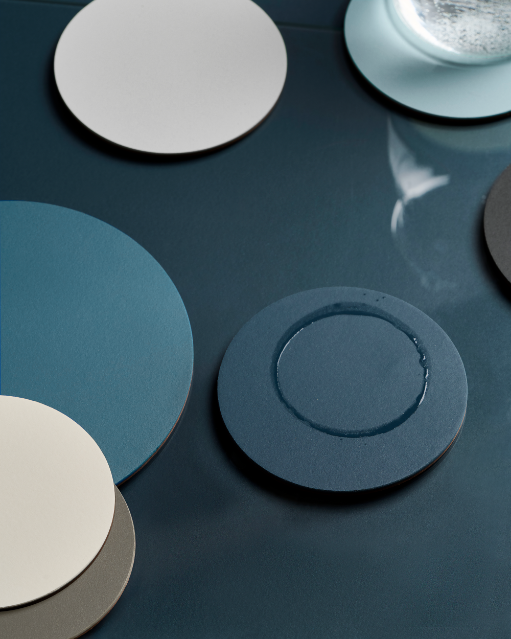 PAD coasters made of linoleum in cool blue tones arranged on a dark blue linoleum tray.