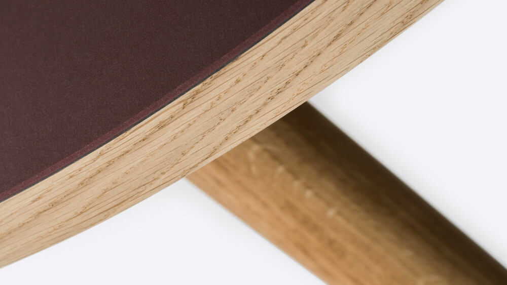 Detail of a round wooden tabletop lined in Burgundy linoleum and mounted on MT2 oak legs by Murken Hansen for FAUST Linoleum