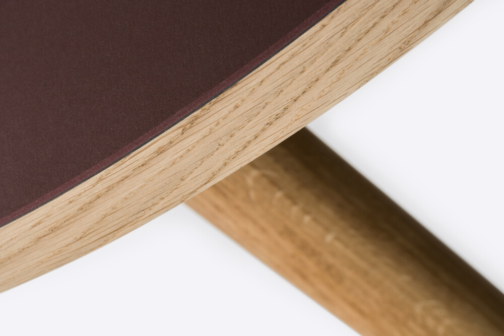 Detail einer runden, mit burgunderfarbenem Linoleum beschichteten Holztischplatte auf MT2-Eichenbeinen von Murken Hansen für FAUST Linoleum