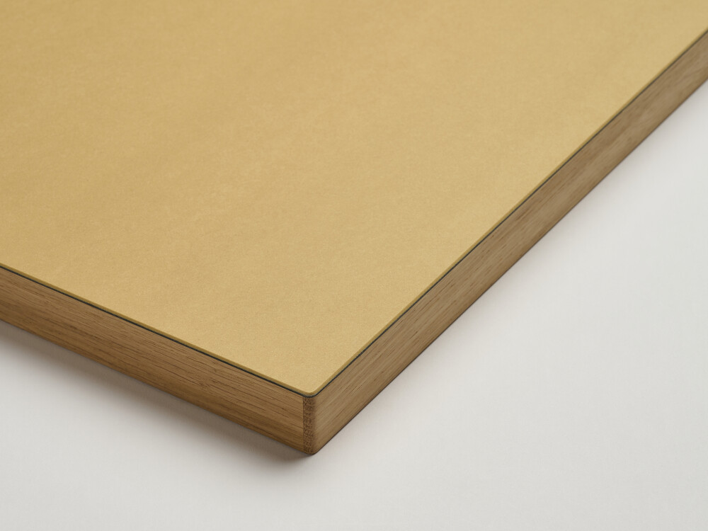 Nahaufnahme einer eckigen Faust-Tischplatte mit matter Linoleumoberfläche in Ockergelb und gerader Eichenholzkante mit natürlicher Struktu