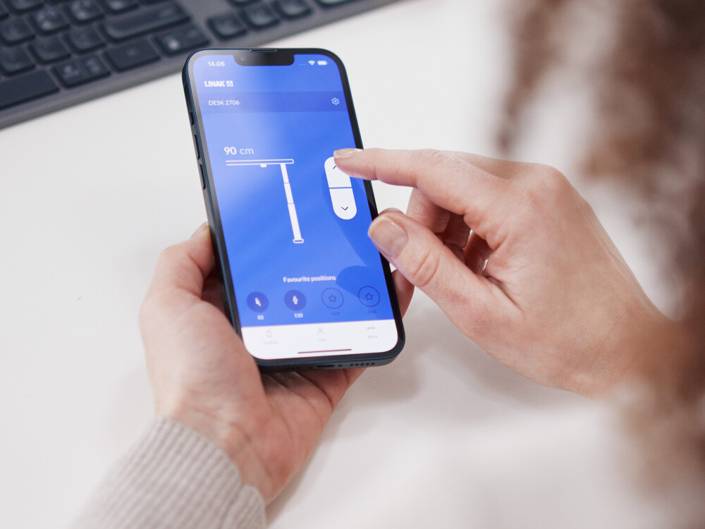 A person controls the height of an ATS desk by Michel Charlot via the LINAK app on their smartphone.