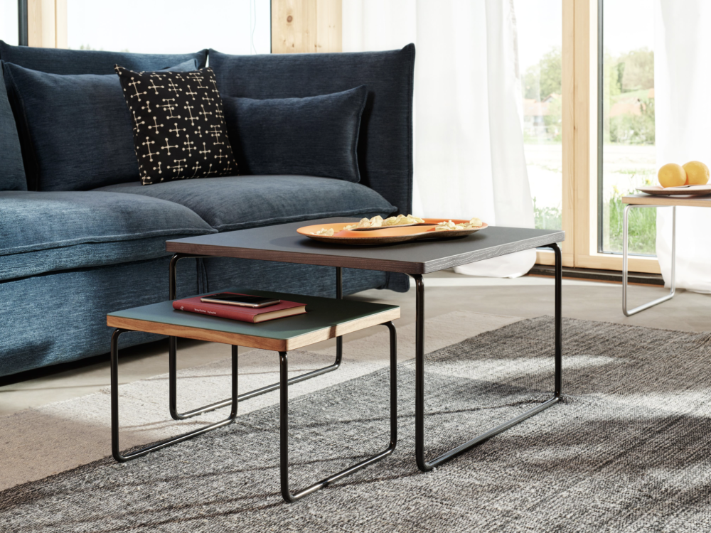 Two Low & Lower side tables by Faust, arranged one on top of the other, placed in front of a blue sofa in a living room.