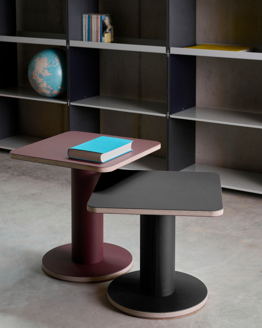 Two OFF-CUT side tables by Faust with square linoleum tops in burgundy and black, placed in the living area.