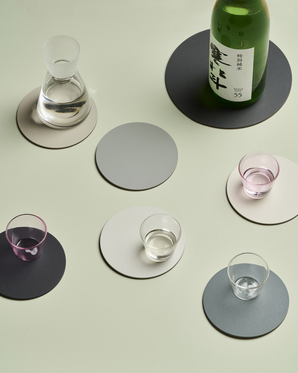 PAD coasters made of linoleum in cool grey tones on a light green table surface, arranged with glasses and a bottle.