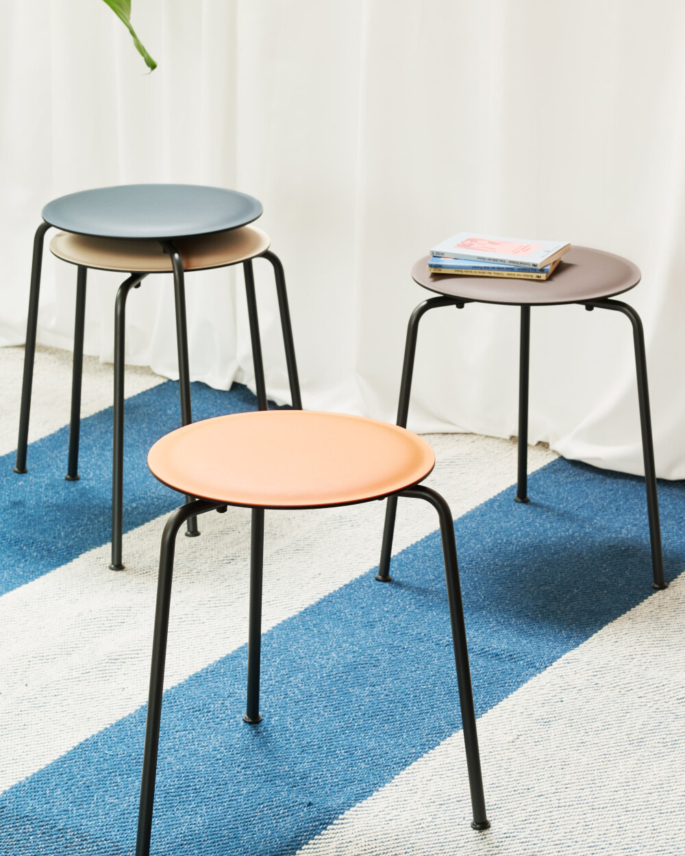 RAVIOLI stool with linoleum seats in various colours on a blue and white carpet in front of light-coloured curtains.