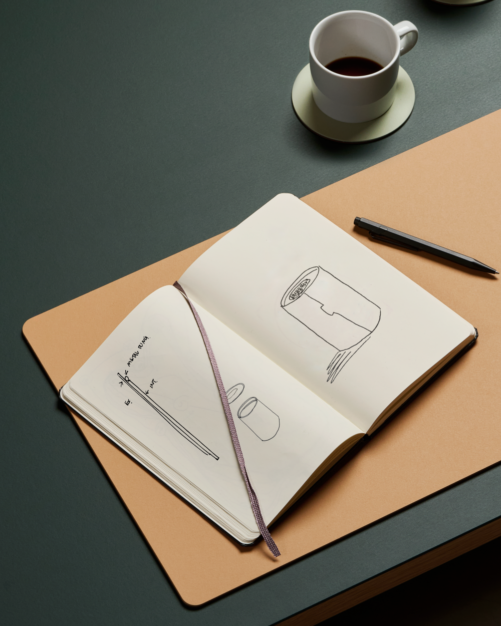 PAD desk pad made of linoleum in leather colour with open sketchbook, pen and coffee cup on dark table surface.